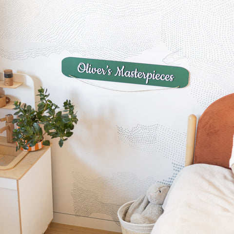 Children's room with a sign reading 'Oliver's Masterpieces' on a textured wall.