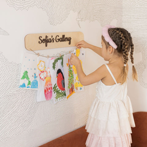 Child hanging drawings on a wall with 'Sofia's Gallery' sign