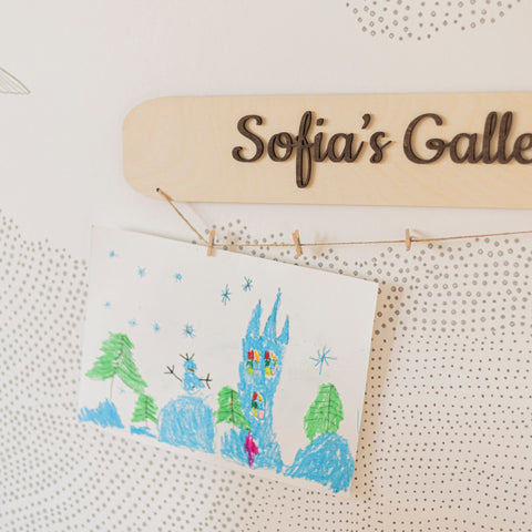 Cross-stitched scene of a castle with trees, hanging on a wooden nameplate with 'Sofia's Gallery' engraved.