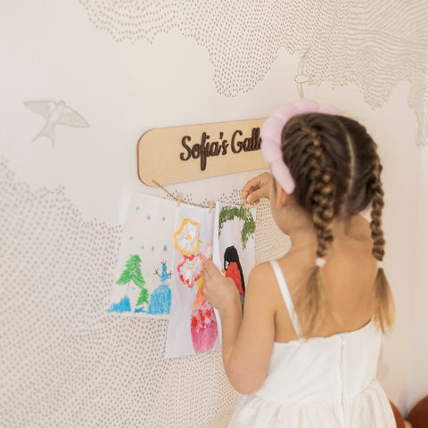 Child with braided hair and a pink hair accessory looking at drawings on a wall-mounted board.