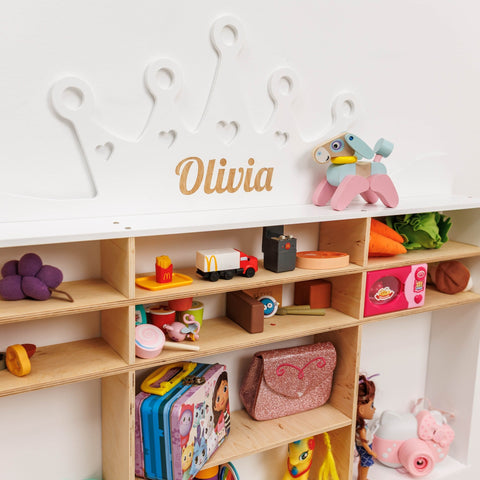 Children's toy shelf with various toys and a personalized name plaque on a white wall.