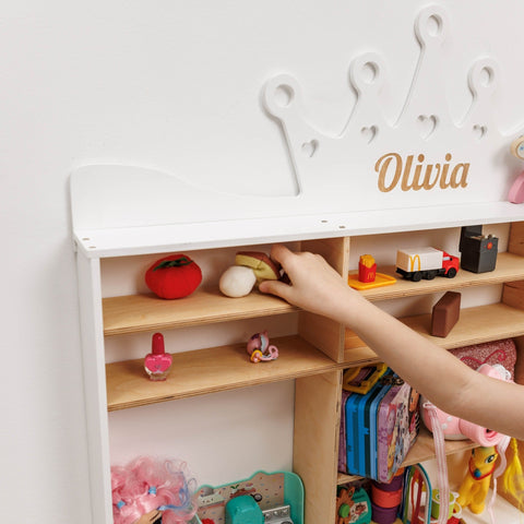 Children's toy shelf with various toys and a hand reaching for a toy, personalized with 'Olivia'.