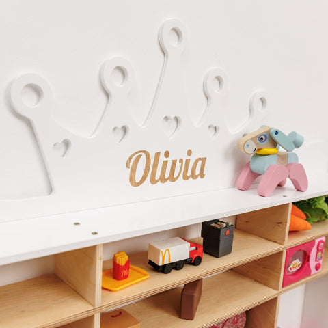 Children's toy shelf with a nameplate reading 'Olivia' and various toys on a white background.