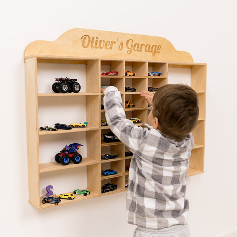 Child playing with a wooden toy car garage named 'Oliver's Garage' on a white background.