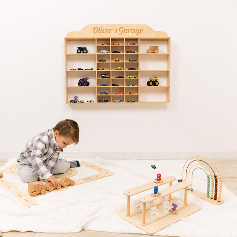 Child playing with wooden toys in front of a shelf labeled 'Oliver's Garage' filled with toy cars.