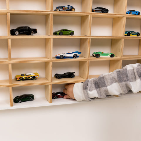 Wooden shelf with model cars and a hand reaching out to pick one up.